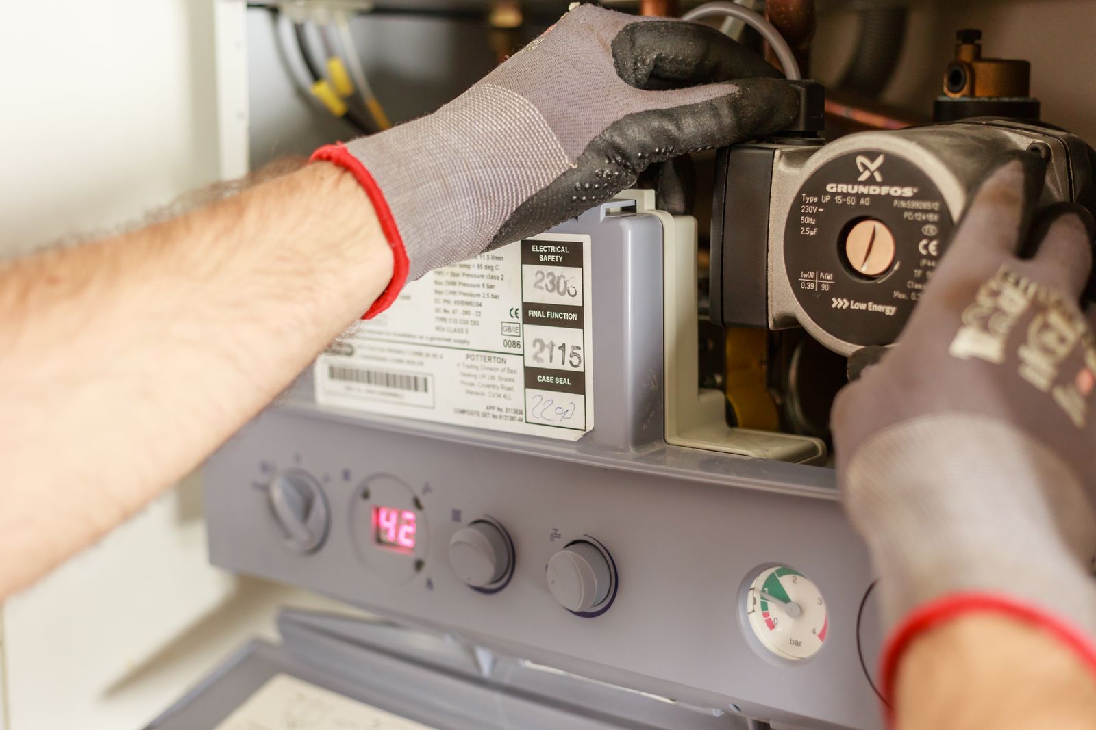 Gloved hands adjusting the pump on a boiler