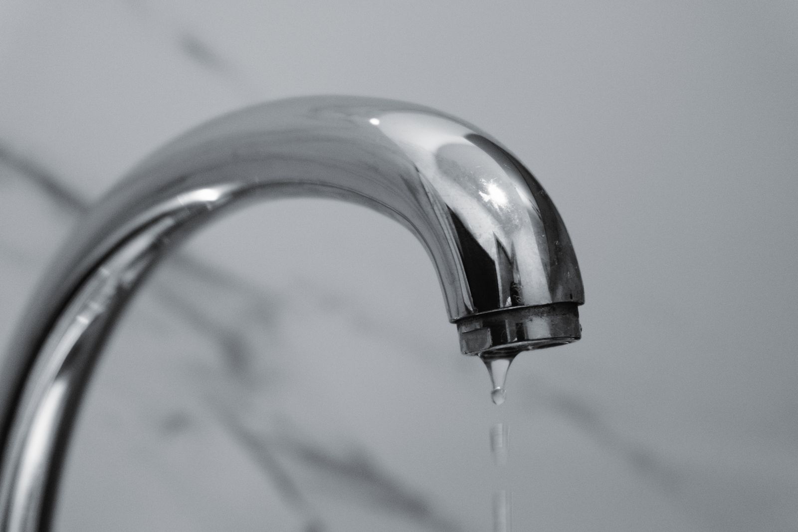 A chrome faucet with a drop of water falling from the spout