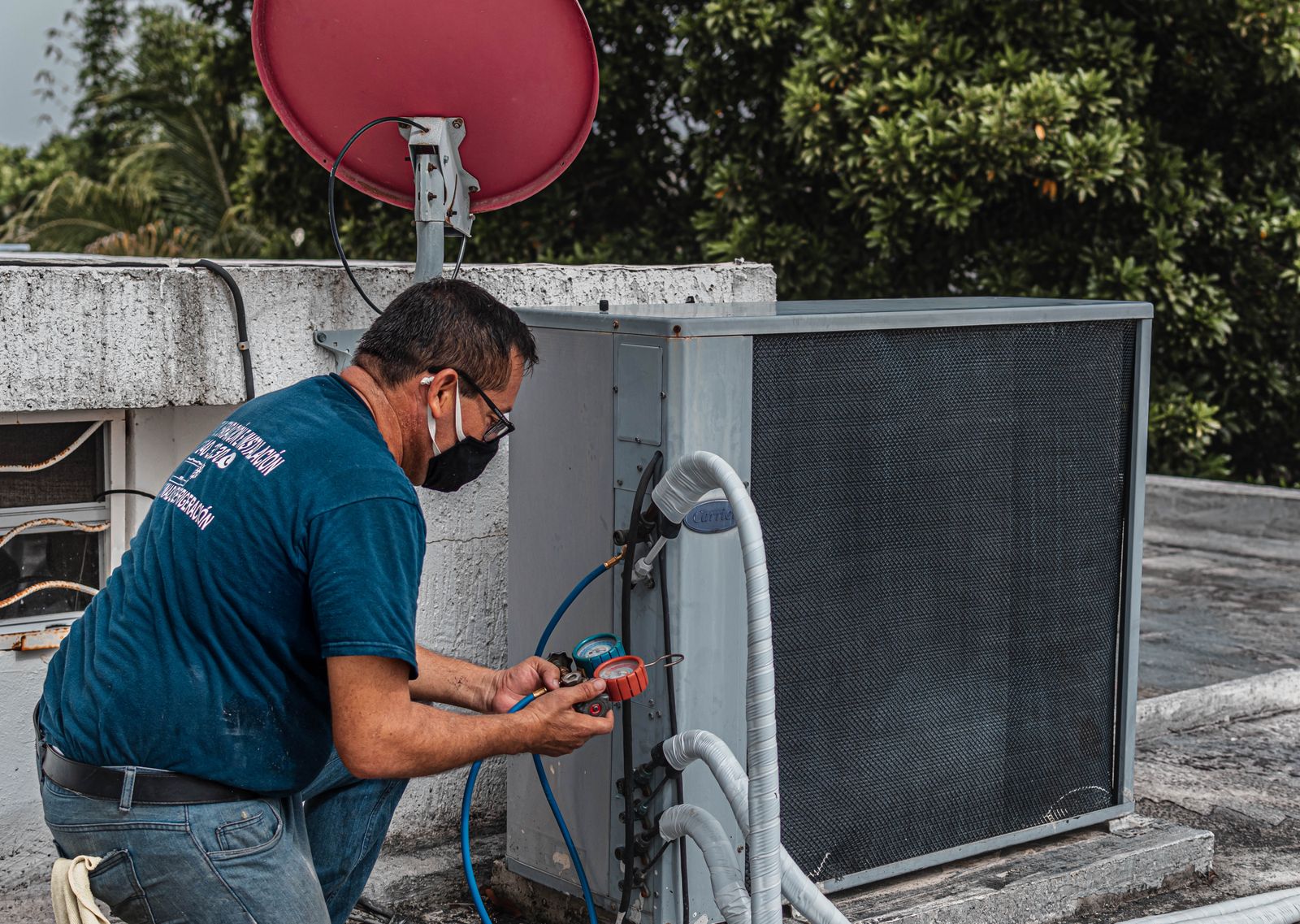 A technician in a face mask checking refrigerant pressure with gauges at an outdoor air conditioner