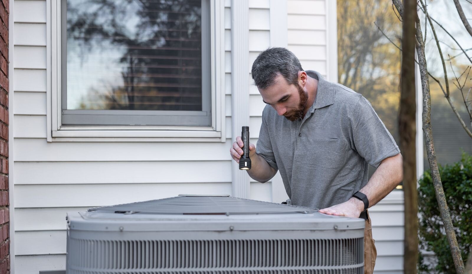 A technician checking the top of an outdoor air conditioner with a flashlight