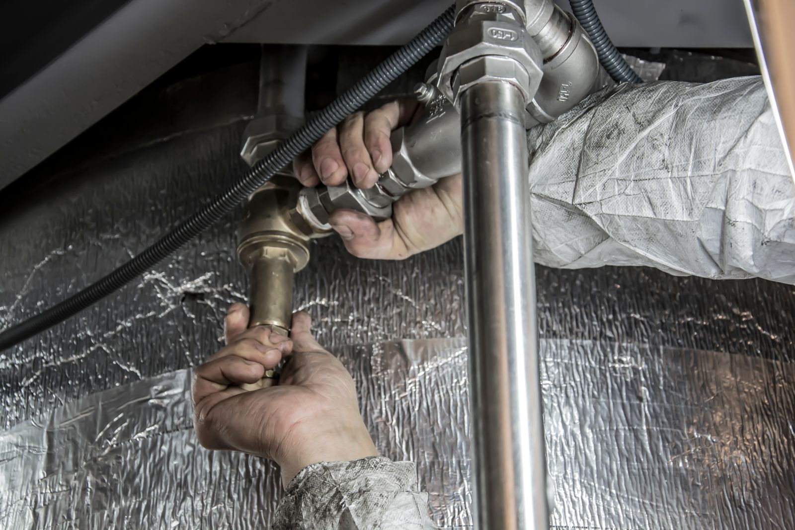 A plumber’s hands tightening a brass fitting on an insulated pipe