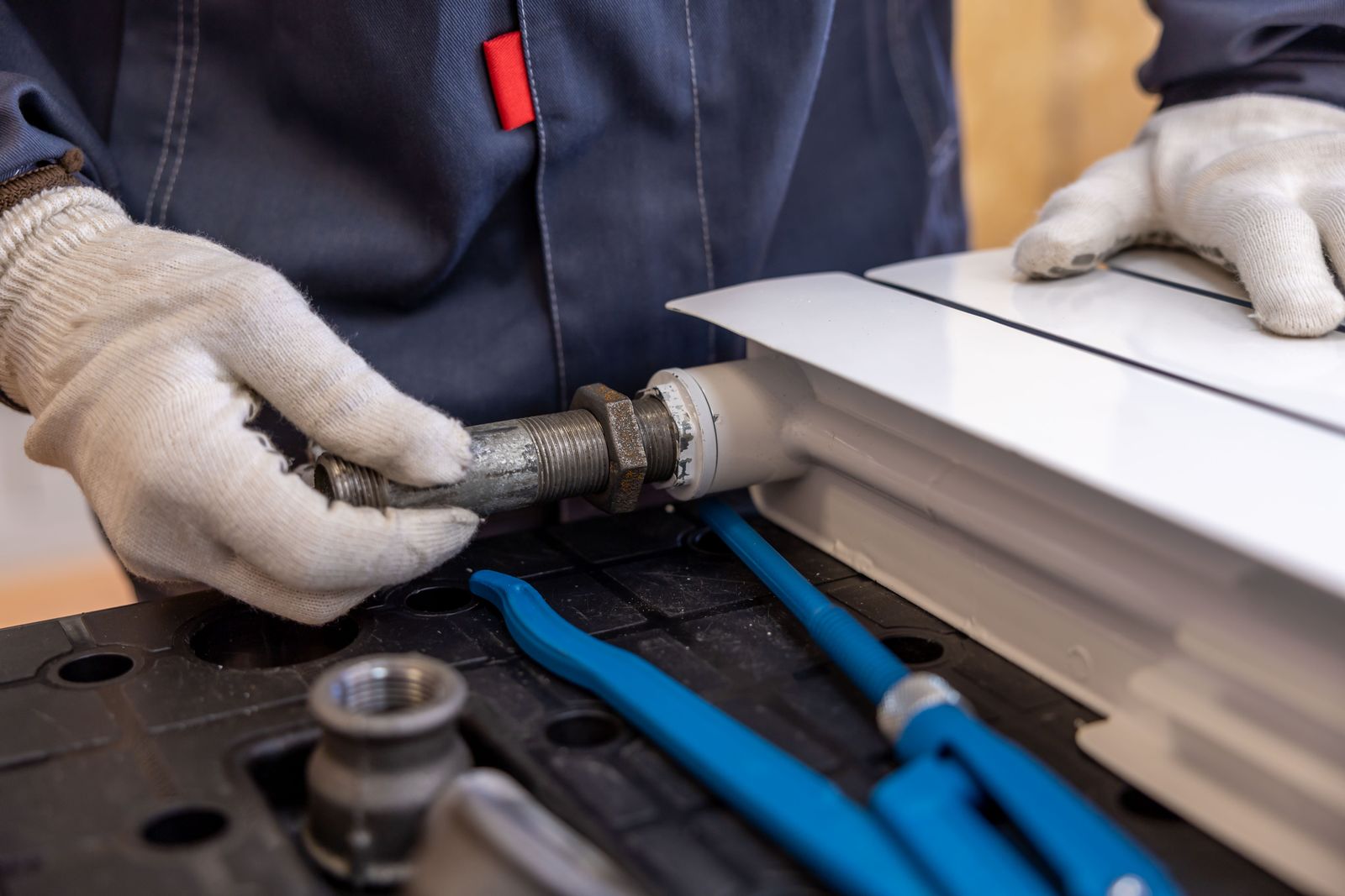 Gloved hands connecting a pipe to a white radiator