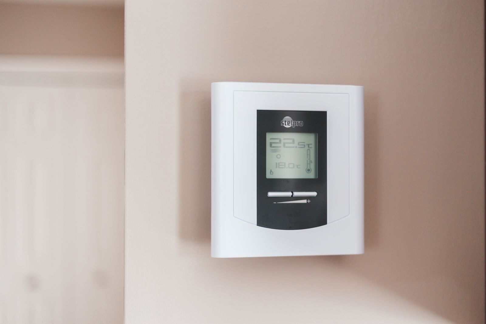 A digital thermostat mounted on a painted wall