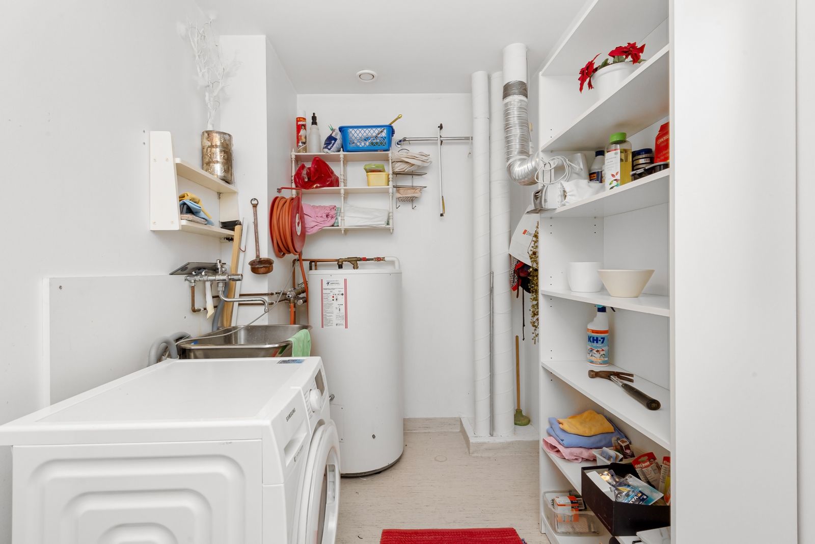 A tank water heater in a laundry room with exposed pipes